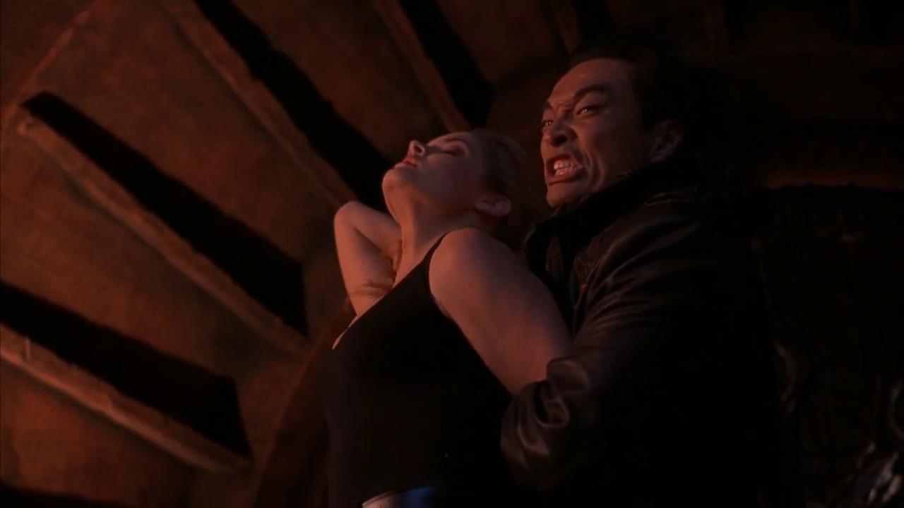 Intense scene showing Shang Tsung gripping Sonya Blade in a dark lair, as he menacingly restrains her while she struggles