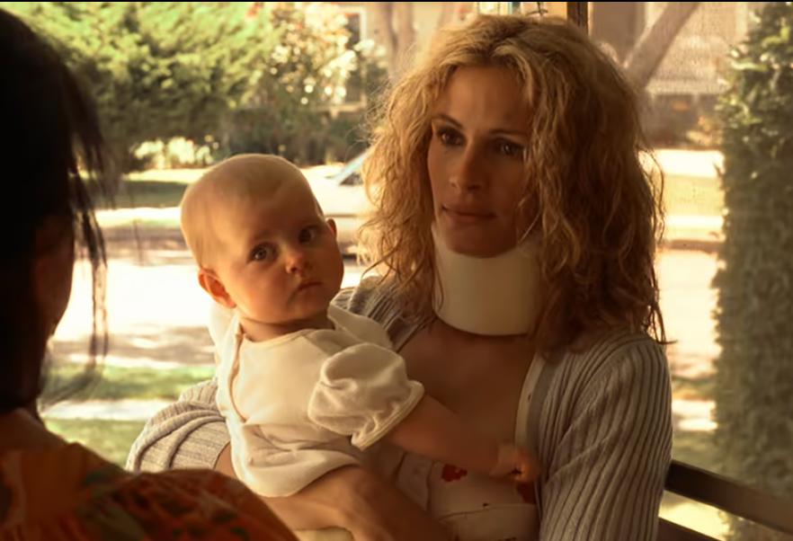 Julia Roberts as Erin Brockovich, wearing a neck brace and holding a baby, depicting her struggles as a single mother while uncovering a major corporate cover-up