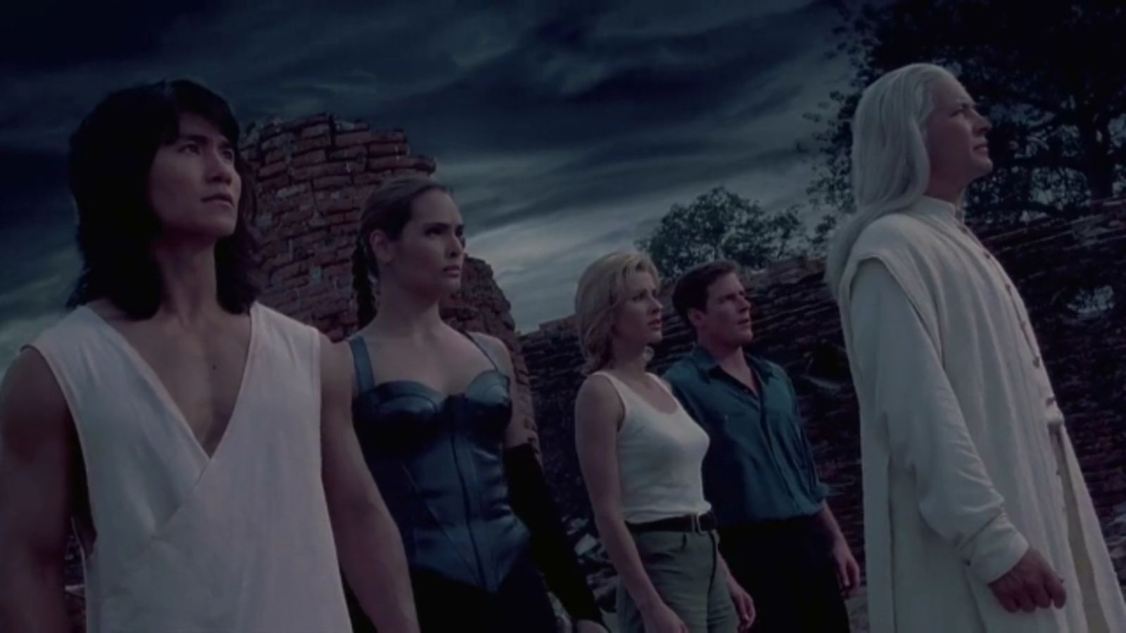 Liu Kang, Kitana, Sonya Blade, Jax, and Raiden standing together in front of ancient ruins under a dark stormy sky.